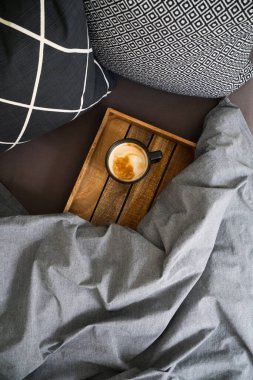 Siyah bir fincan kahve siyah defter üzerinde ahşap tepsi üzerinde gri battaniye ve siyah beyaz yastıklar ile yatakta. Sabah ayini. Üst görünüm.