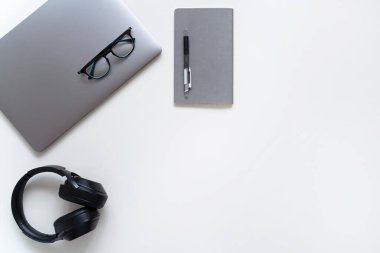 Online eğitim. Laptop, gözlük, defter, kalem ve kulaklıklar beyaz masada. Metin için alanı kopyala.