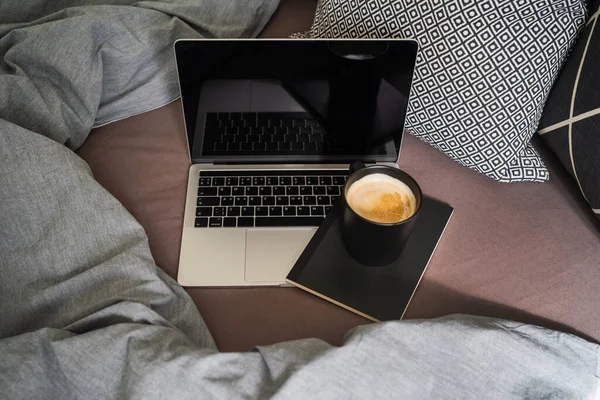 Laptop with notebook and cup of coffee on bed. Work at home.