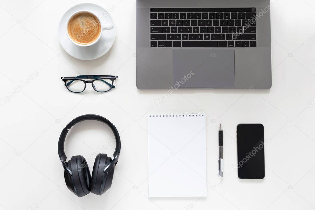 Online office. Laptop, glasses, cup of coffee, mobile phone, notebook and headphones on white table. Knolling.