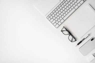 Blogcu çalışma masası. Cep telefonu, klavye, dokunmatik ped, kalem, defter, şarj aleti ve gözlük. Düğümleniyor.