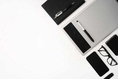 Üst görünüm beyaz çalışma masası. Çalışma alanı, defter, kalem, tablet, gözlük, cep telefonu, flash disk ve güç bankası. Boşluğu kopyala.