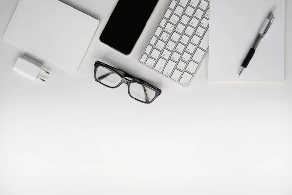 White workplace. Mobile phone, keyboard, touchpad, pen, notebook, charger and glasses. Copy space.