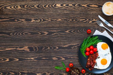 Amerikan kahvaltısı omlet, pastırma, taze vişneli domates roka ve çatal ve bıçakla servis edilen ahşap masada servis edilen bir fincan kahve. Düz yatıyordu. Boşluğu kopyala.