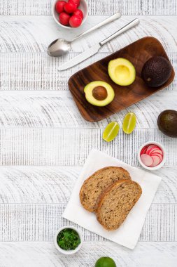 Taze çavdar ekmeği, limon, ot, turp, avokado, kaşık ve bıçak dilimleri beyaz ahşap masada. Sağlıklı kahvaltı. Üst görünüm.