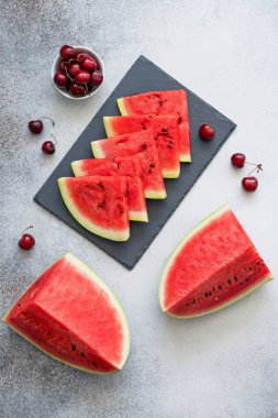 Siyah tabakta karpuz dilimleri, kirazlar ve beton zeminde karpuz parçaları. Düz yatıyordu.