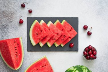 Siyah tabakta karpuz dilimleri, kirazlar ve beton zeminde karpuz parçaları. Düz yatıyordu.