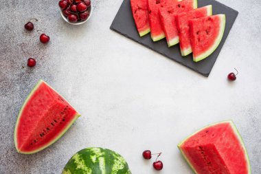 Yaz çilekleri çerçevesi. Karpuz dilimleri o siyah tabak, kirazlar ve karpuz parçaları beton arka plan. Uzayı kopyala Üst görünüm.