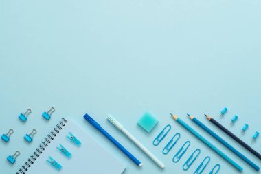 Okul konseptine geri dönelim. Mavi arka planda mavi kırtasiye seti. Kağıt raptiyeler, defter, keçeli kalemler, silgi, ataç ve kalemler. Knolling. Boşluğu kopyala.
