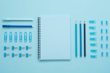 Kırtasiye seti mavi arkaplanda. Kağıt raptiyeler, defter, keçeli kalemler, silgi, ataç ve kalemler. Okula dönelim. Düğümleniyor. 