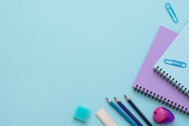 Eğitim düzlüğü. Mavi ve mor defterlerin üst görünümü, kalem açacağı, ataçlar, silgi, cetvel ve renkli kalemler. Boşluğu kopyala. 