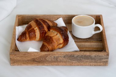 Taze pişmiş kruvasan ve beyaz yataktaki ahşap tepside bir fincan kahve. Yatakta kahvaltı.. 