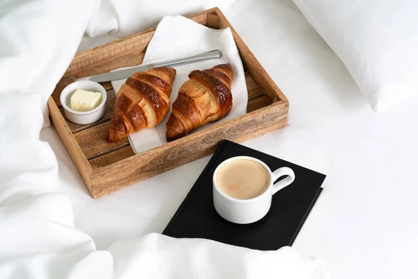 木製のトレイに2つのクロワッサンとバターとベッドで朝食 コーヒーカップと枕と毛布とホワイトシートの本 Instagram Style — ストック写真