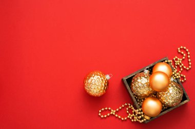 Noel süsleri. Kırmızı arka planda, ahşap kutuda altın takılar ve boncuklar var. Yeni yıl süslemeleri.