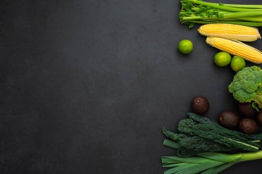 Siyah arka planda yeşil sebzelerin fotokopi alanı ile üst görüntüsü. Kereviz, mısır, brokoli, avokado, lahana, pırasa ve limon. Sağlıklı yaşam tarzı.
