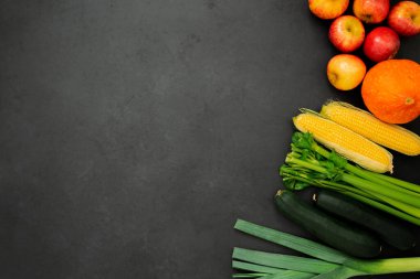 Çeşitli meyve ve sebzelerin üst görüntüsü. Pırasa, kabak, kereviz, mısır, balkabağı ve elmalar siyah zemin üzerinde fotokopi alanı. 