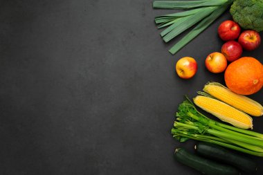 Çeşitli meyve ve sebzelerin üst görüntüsü. Siyah arkaplanda pırasa, kabak, kereviz, mısır, balkabağı, elma ve brokoli.. 
