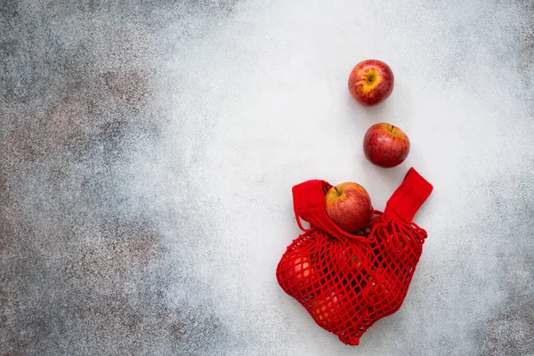 Kırmızı elmalar beton arka planda kırmızı iplik alışveriş torbası. Sıfır atık. Sonbahar meyveleri. 