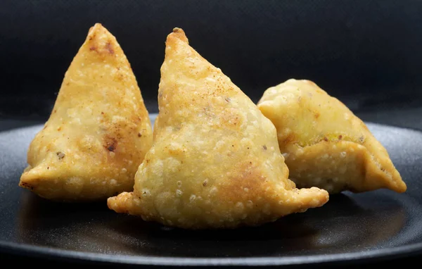 Siyah bir tabakta üç altın rengi samosa. Popüler Hint yemeği..