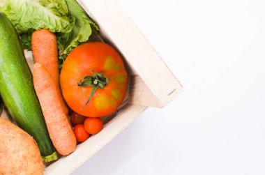 Tahta bir kutunun içinde sebze ve sebzeler. Domates, havuç, kabak ve marul. Beyaz arkaplan
