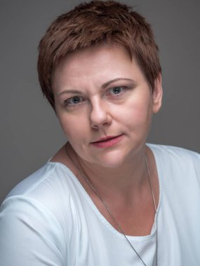 Kafası karışmış, şaşırmış ve gözleri açık bir kadın portresi. Gri arka planda kısa saçlı tombul kadın..