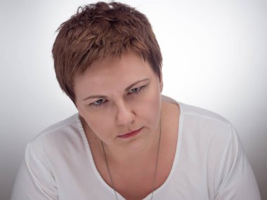 Yüzünde yoğun, esrarengiz bir ifade olan kadın portresi. Kısa kahverengi saçlı, beyaz bir kadın..