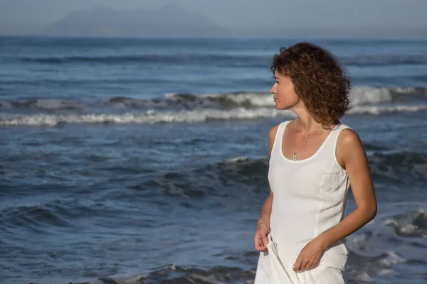 Mujer joven en vestido blanco caminando cerca de una playa en un día soleado de verano Imagen De Stock