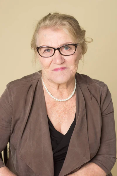 Portrait of an old woman wearing glasses on a beige background