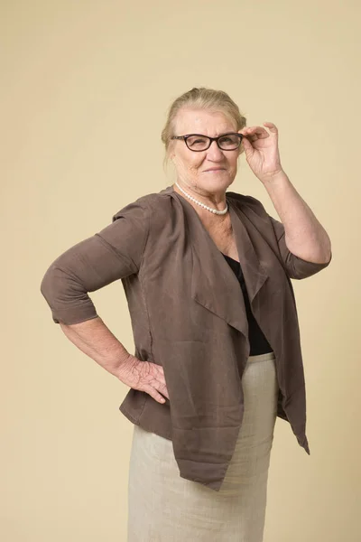 Portrait of an old woman wearing glasses on a beige background