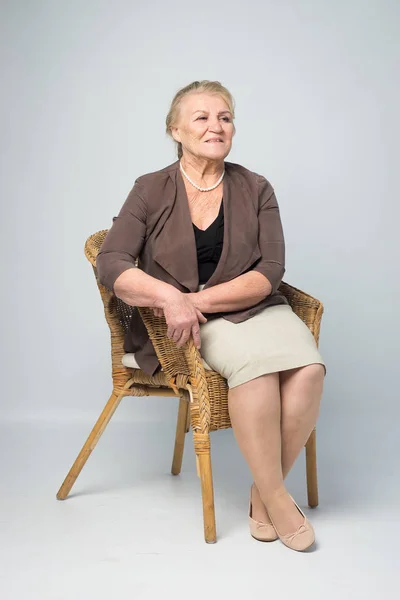 在白色背景的柳条椅子上的老妇人的肖像 — 图库照片