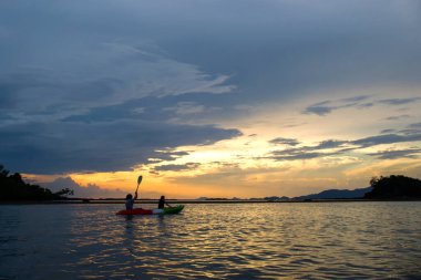 Denizde kayak yapan bir çift, batan güneşin gölgesinde