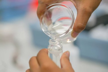 Bilim adamı Erlenmeyer şişesinden ölçüm tüpüne sıvı döküyor. Elleri ve camları kapatın..