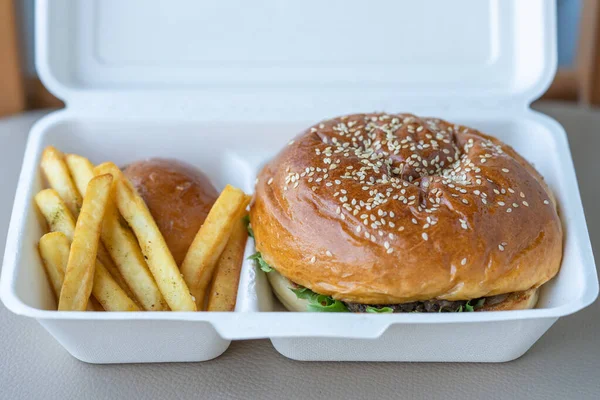 Burger with meat and French fries in paper box for the delivery.