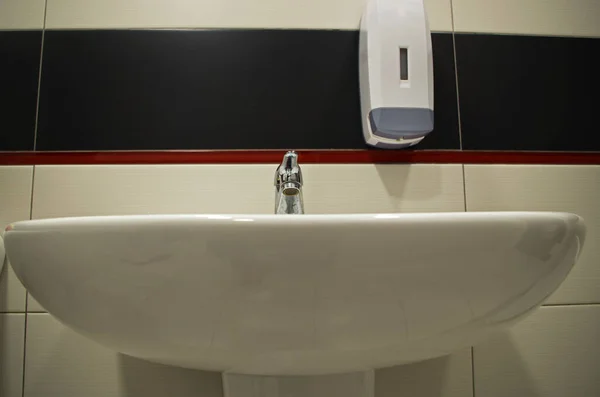 白いセラミックシンクの上のクロム蛇口と機関 設立またはオフィスの洗面所やトイレのタイルの壁をトリミング白い黒い赤いストライプに液体石鹸のハンギングコンテナ — ストック写真
