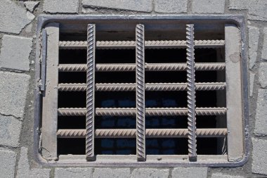 Oluklu güçlendirme parmaklıklarından kaynaklanan metal ızgara, fırtına kanalizasyon kuyusunun üstündeki gri fayanslı kaldırımda uzanıyor, derinlerde görülebilen su. Kavram: Şehrin kaldırımlarının sağanak yağmurlardan korunması.