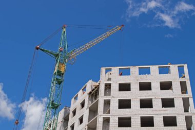 Sarı kabini olan yeşil kule vinci, kırmızı vinçleri olan flok yelkeni ve açık mavi gökyüzüne karşı beyaz tuğlalardan oluşan en üst kattaki inşaat alanında çalışan bir kanca.