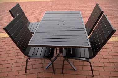 Tahta siyah masa ve yaz mevsiminde kırmızı şeritli sarı şeritli kırmızı kafenin terasında metal bacaklı dört siyah sandalye.