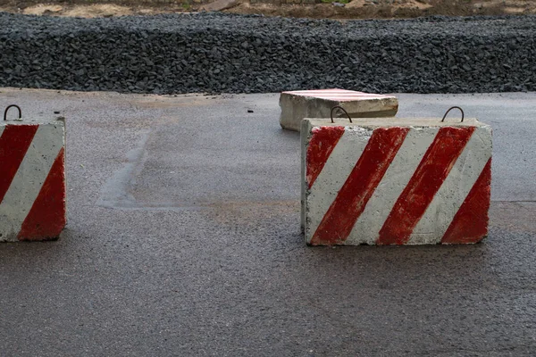 In connection with the road works, the road is closed with reinforced concrete slabs painted in a warning pattern with diagonal red and white stripes, behind them rubble for the road surface is piled