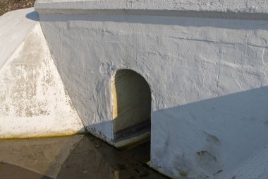 Boyanmış beyaz beton drenaj hendeği tasarımı altında kemer şeklinde bir delik var. Altında yol veya demiryolu yüzeyinde yağmur suyu var. Kavram: yolu boğulmaktan korumak