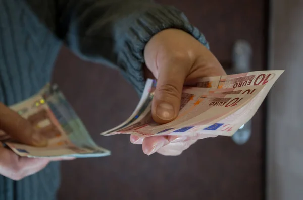 Gri örgü süveterli bir kadın, sol eli kahverengi ön kapıya dayanmış üç tane on avroluk banknot tutuyor. Kurucu, tesisatçı ya da elektrikçi dairede bakım için ödeme
