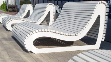 Bir sıra beyaz ahşap sıra sıra sıra sıra sıra sıra sıra sıra dizilmiş yuvarlak şekilli, arkasında cam pavyonun arka planında kaplama karoları olan bir plaj şına benziyor.