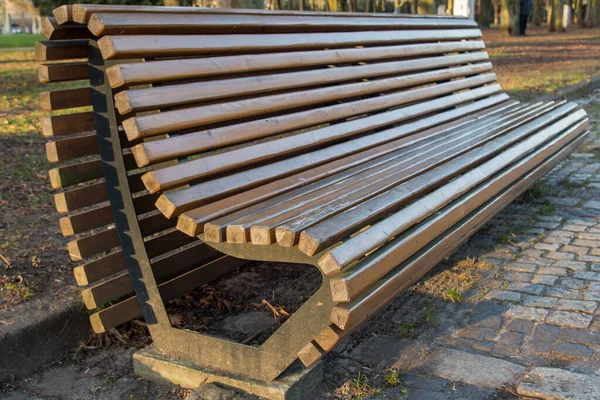 Metal kenarlı ahşap bir bank, bir yanda kalp şeklinde, kaldırımın önündeki taş kaldırımda duran arka plandaki çimlere karşı sabah altın saatinde parkta.