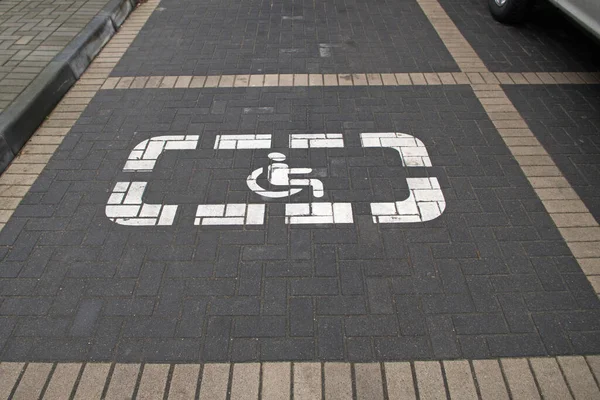 A space marked with a white disabled parking symbol painted in white and delimited by a light beige tile on a gray sidewalk parking lot near by the institution