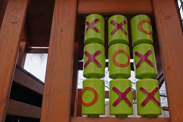 論理ゲーム チックタックトゥ はしごやプラットフォームの木製の構造の形で子供の遊び場に緑のシリンダーに適用される赤とオレンジのシンボルで実装された3行のゲームの一種 — ストック写真