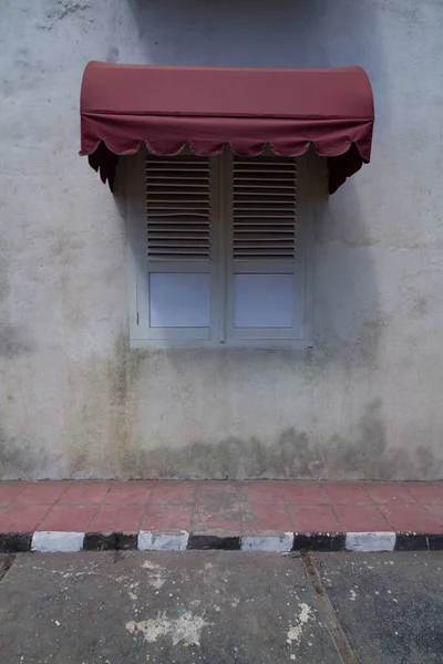 red awning over the window on concrete wall of old bulding