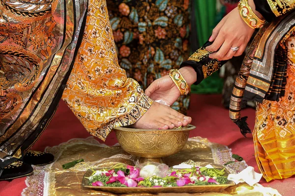 bride washing groom feet at traditional javanese wedding ceremony