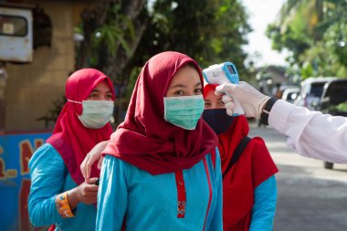 Müslüman Endonezyalı kadın maske takıyor ve vücut ısısını kontrol ediyor. Covid 19 protokolü. Corona virüsü salgını - Yogyakarta, 9 Temmuz 2020