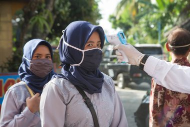 Müslüman Endonezyalı kadın maske takıyor ve vücut ısısını kontrol ediyor. Covid 19 protokolü. Corona virüsü salgını - Yogyakarta, 9 Temmuz 2020