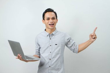 Asyalı mutlu adam dizüstü bilgisayarı tutuyor ve arka planda parmak işareti yapıyor.