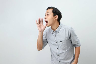 Genç Asyalı Endonezyalı bağırıyor ve izole edilmiş arka planda elleri ağızlarına dolanıyor.